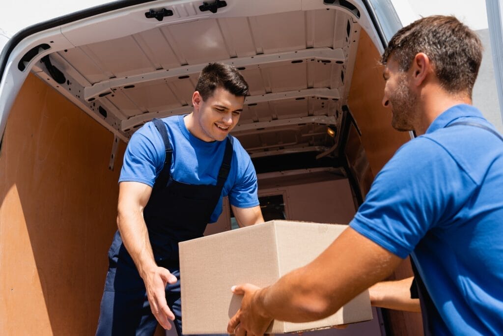 Movers unloading a truck filled with cardboard boxes on an urban street, showcasing the moving process in a city environment.